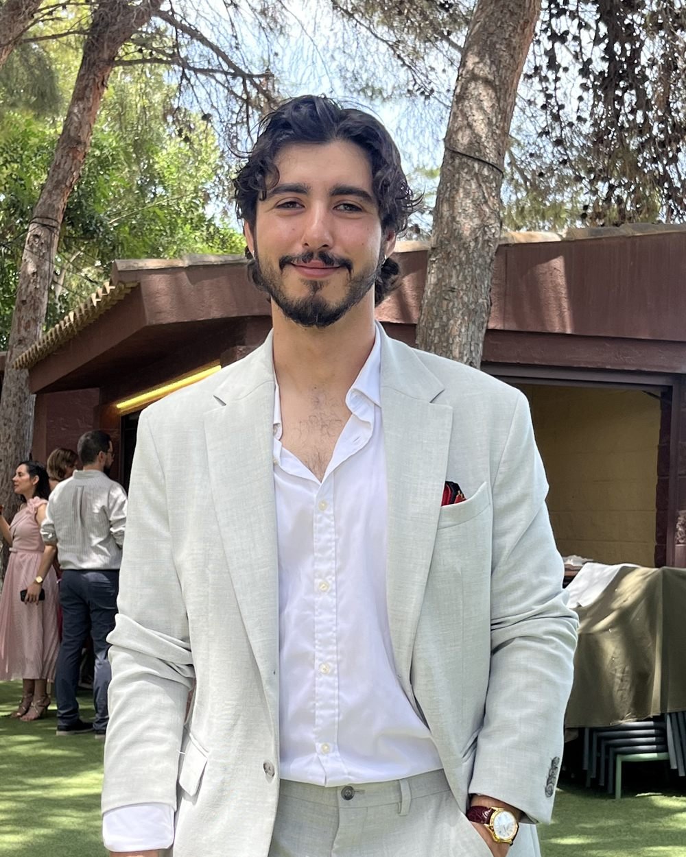 Aaron Nieto con traje claro y camisa blanca, sonriendo a cámara al aire libre.